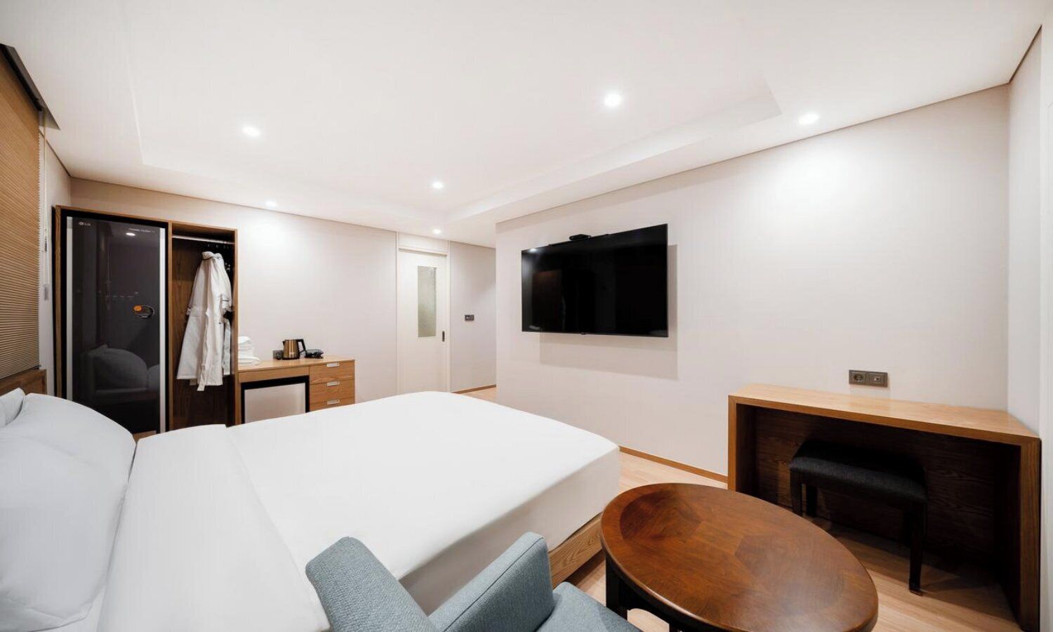 Moderni hotellihuone, jossa on suuri sänky, työpöytä, tuoli ja seinälle asennettu televisio.