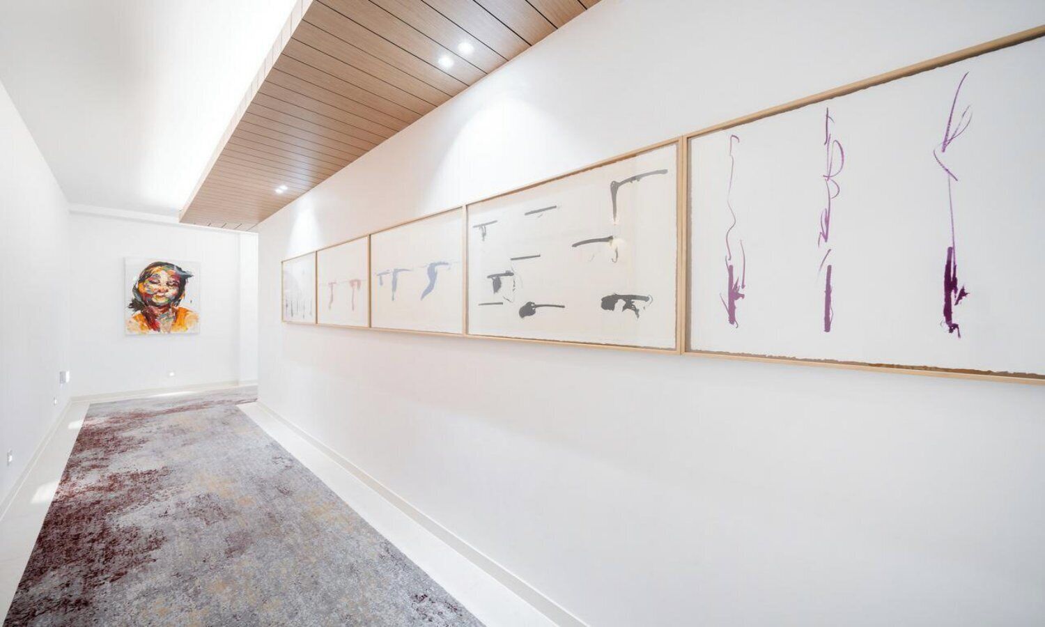Un corridoio con pareti bianche e soffitto in legno, con una serie di opere d'arte incorniciate sulla parete destra.