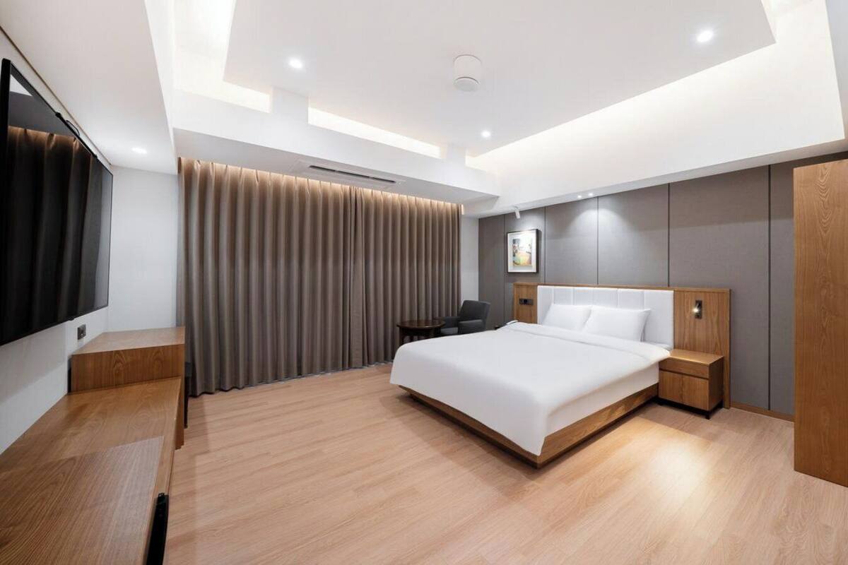 A modern hotel room with a large bed, a desk, a chair, a TV, and a wardrobe.
