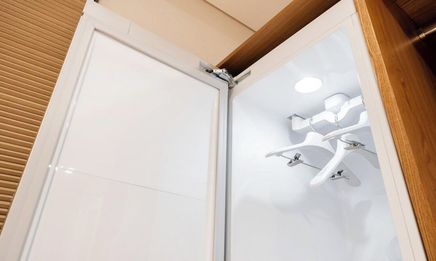 A corner of a room with a white door and a shower area with a white ceiling and a wooden ceiling beam.
