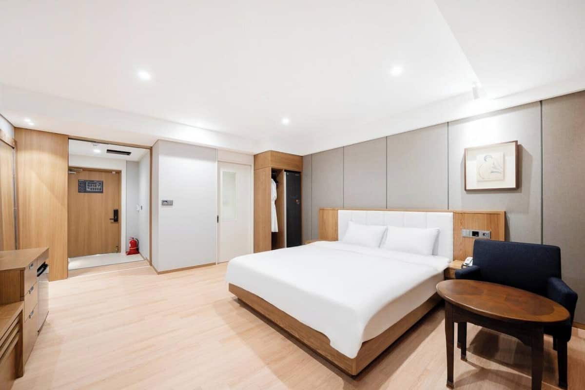 A modern hotel room with a large bed, a desk, a chair, and a small table.