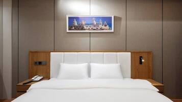 A hotel room with a large bed, a bedside phone, a framed artwork above the bed, and a wooden headboard.