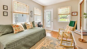 A bedroom with a bed, a rocking chair, a door, and windows with blinds. - Near Horse Shows & Events! Blissful Tryon Cottage (Tryon)