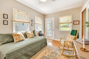 A bedroom with a bed, a rocking chair, a door, and windows with blinds.