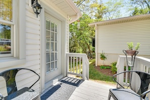 A porch with two chairs, a door with a window, and a small shed with plants.