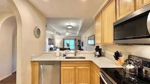 A modern kitchen with wooden cabinets, stainless steel appliances, and a large TV. - Comfy Cove Resort Stay for 8 (Kissimmee)