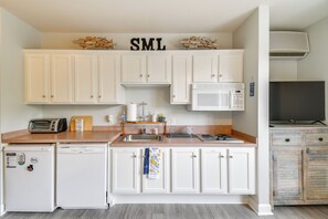 Una cocina compacta con armarios blancos, microondas, tostadora y lavavajillas.