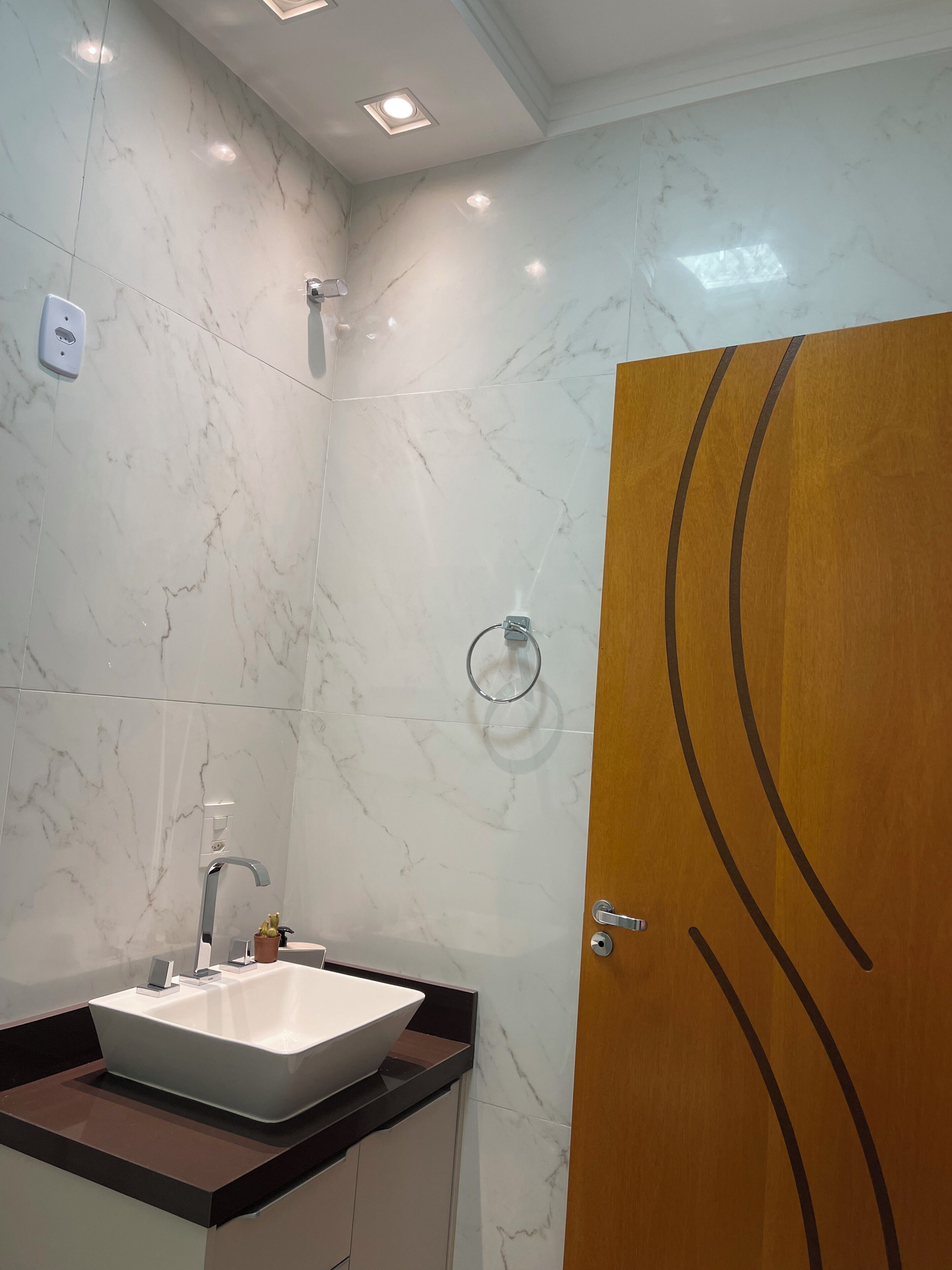 A bathroom with a marble wall, a sink, a shower, and a wooden door.
