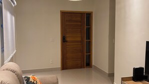 A modern living room with a sofa, a patterned rug, a wooden door, and recessed ceiling lighting. - Lilly Queen I, 3-bedroom house in adorable Londrina with AC near to the Airport (Londrina)