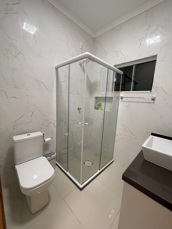 A bathroom with a toilet, a glass-enclosed shower, and a sink.