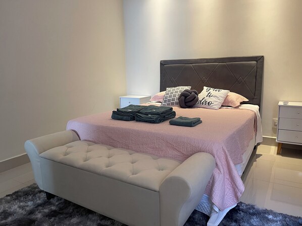 A neatly made bed with a pink bedspread, a tufted headboard, and a bedside table with a lamp.
