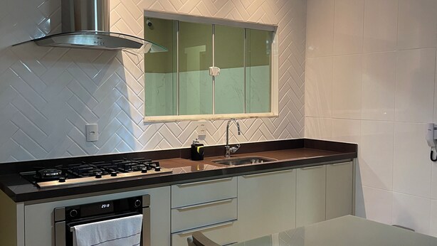 A modern kitchen with a gas stove, stainless steel range hood, and a glass island with a sink. - Lilly Queen I, 3-bedroom house in adorable Londrina with AC near to the Airport (Londrina)
