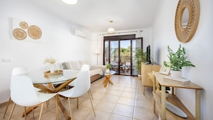 A modern living room with a glass dining table, white chairs, a sofa, and a balcony with a view. - Barrosa Beach Apartment -Chiclana de la Frontera (Chiclana de la Frontera)