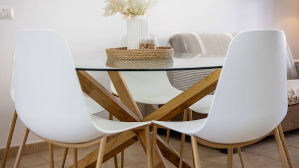 A dining area with a glass table, white chairs, and a woven basket centerpiece. - Barrosa Beach Apartment -Chiclana de la Frontera (Chiclana de la Frontera)