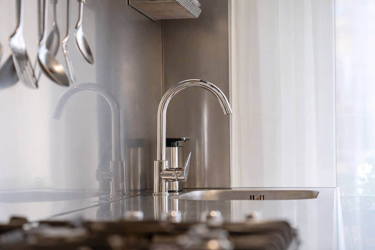 A modern kitchen with stainless steel appliances, a sleek faucet, and hanging utensils.