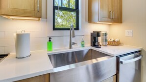 A modern kitchen with a stainless steel sink, wooden cabinets, a window with a view, and a built-in dishwasher. - Walkable North Georgia Hideaway! Modern Suite (Ball Ground)