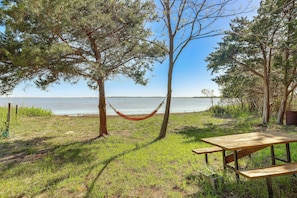 A picnic table and hammock by a lake with trees and grass. - Walk to the Bay! Getaway Near Alligator River (Stumpy Point)
