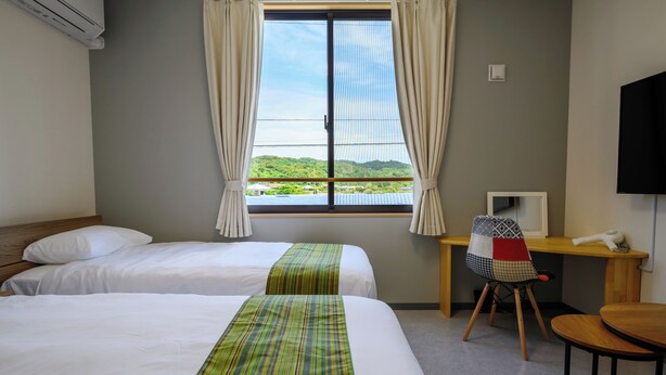 Une chambre d’hôtel avec deux lits, un bureau, une chaise, une télévision et une fenêtre avec des rideaux.