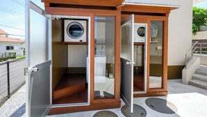 Un espace extérieur compact dédié à la lessive, comprenant deux machines à laver, un espace de séchage et un petit espace clos avec une douche.