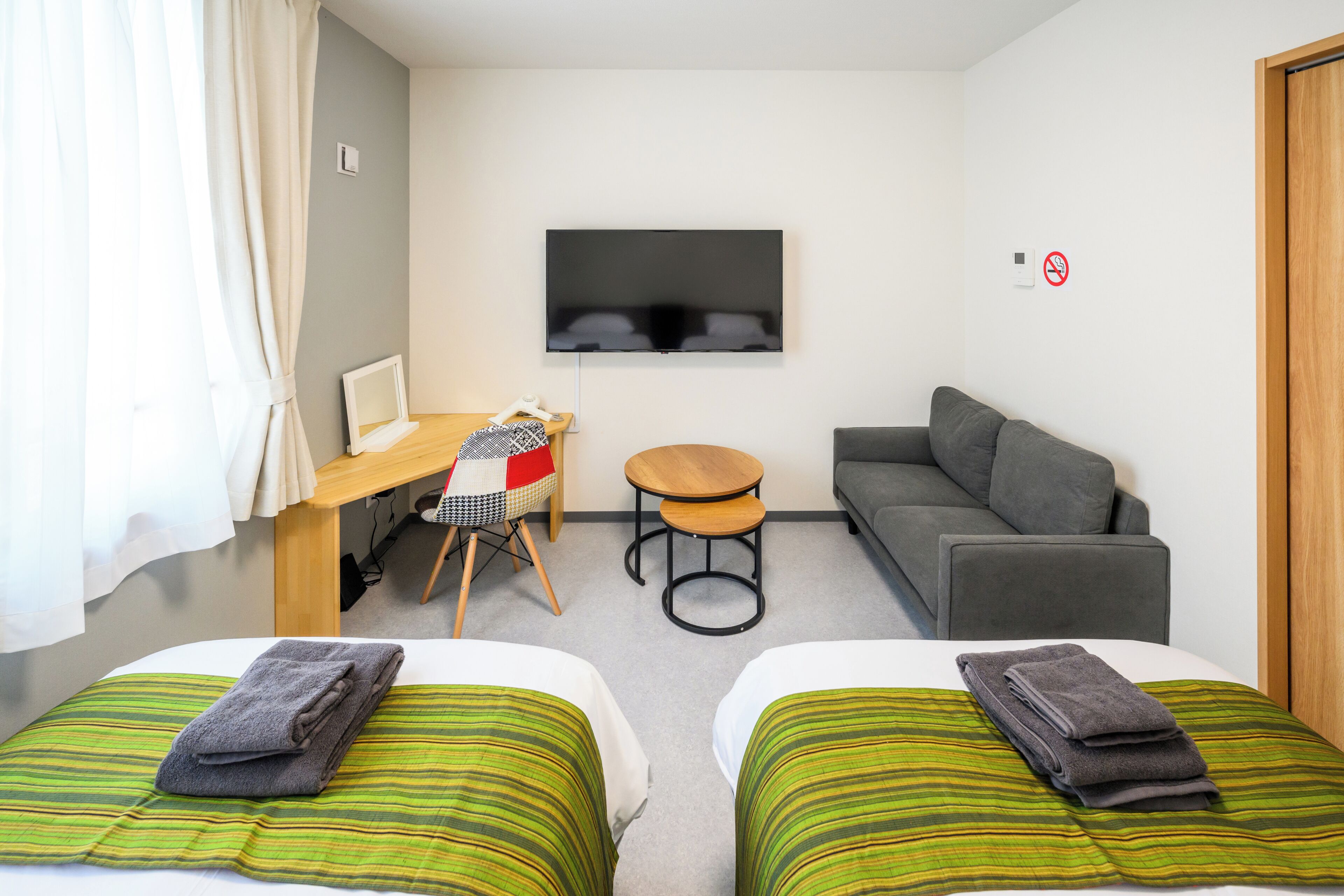 A hotel room with two beds, a TV, a desk with a chair, a small table, and a sofa.