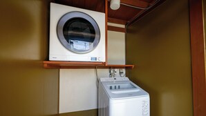 Un espace buanderie compact comprenant un lave-linge à chargement frontal et un sèche-linge à chargement par le haut, tous deux de couleur blanche, dans une pièce aux murs et au plafond en bois.