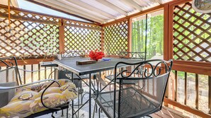 Ein überdachter Patio-Bereich mit Tisch und Stühlen, einer Uhr und Blick auf Bäume.