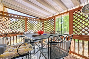 Ein überdachter Patio-Bereich mit Tisch und Stühlen, einer Uhr und Blick auf Bäume.