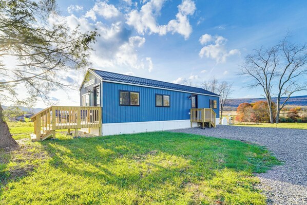 A blue building with a wooden deck, a gravel driveway, and a grassy area. - Little Blue Cabin! Country Stay Near Williamsport (Allenwood)