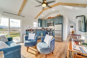 A modern kitchen with teal cabinets, a stainless steel refrigerator, and a dining area with a wooden table and blue chairs. - Little Blue Cabin! Country Stay Near Williamsport (Allenwood)