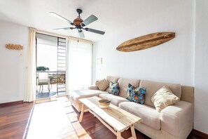 A living room with a sofa, a wooden coffee table, a ceiling fan, and a wooden wall decoration. - Atlantic View Apartment - El Rompido (El Rompido)