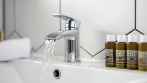 Modernilla hanalla, pesualtaalla ja rivillä hygieniatuotteita varustettu kylpyhuone.