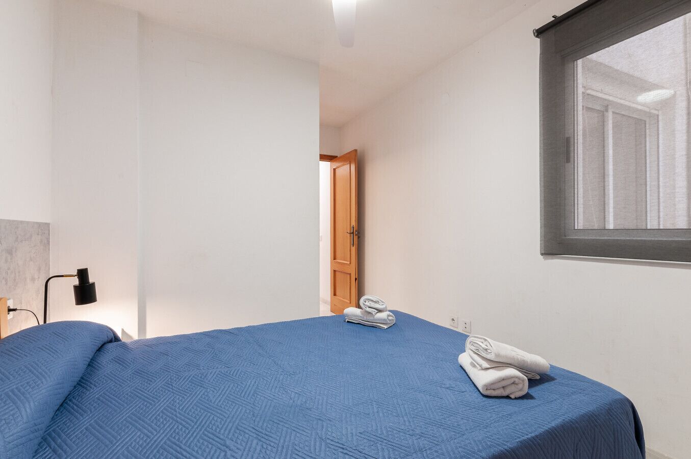Ein Schlafzimmer mit Bett, Fenster, Tür und einer Wandlampe.