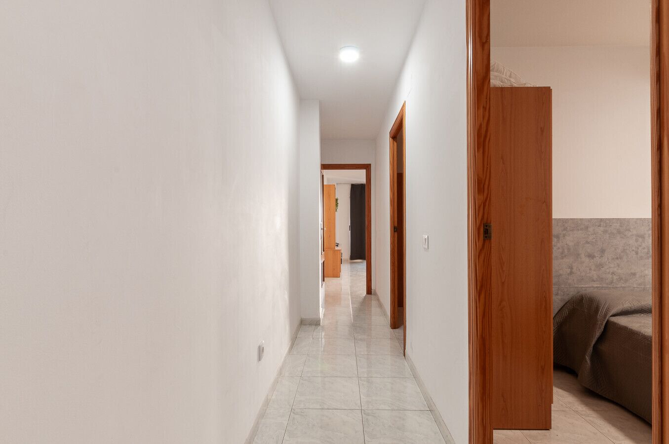 A hallway with a wooden door, a bed, and a tiled floor.