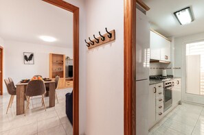 A modern kitchen with white cabinets, a built-in oven, and a dining area with a wooden table and chairs. - Arenal Beach Escape - Burriana Port (Burriana)