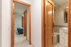 Quarto de hotel com porta de madeira, cama com colcha azul, banheiro com banheira e pia.