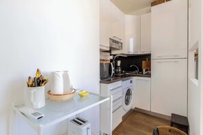 A compact kitchen with white cabinets, a washing machine, a microwave, and a coffee maker. - Air-conditioned Seafront Apartment – Nice (Nice)