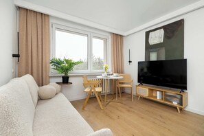 A living room with a sofa, a dining table with chairs, a TV, and a window with curtains. - Comfortable Apartment in Katowice | Close to City Attractions (Katowice)
