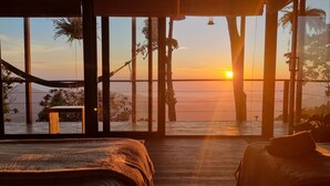 A room with a large window overlooking a body of water during sunset.