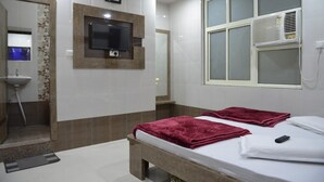 Hotellihuone, jossa on sänky, seinälle asennettu televisio, ilmastointilaite ja peili.