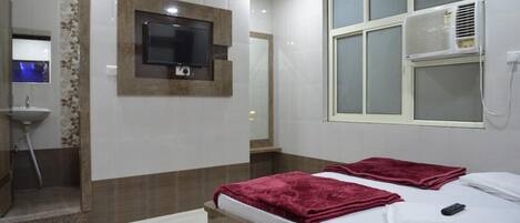A hotel room with a bed, a TV mounted on the wall, an air conditioning unit, and a mirror.