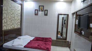 Habitación de hotel con cama, televisión, espejo y baño pequeño.