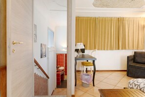 A living room with a sofa, a table, a lamp, and a chair. There is a staircase leading to a bathroom with a red sink. - 7 Archi – 3-Bedroom Apartment in the Heart of Como (Como)