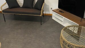 Olohuoneessa on sohva, televisio, lasitasoinen sohvapöytä ja valkoinen kaappi.