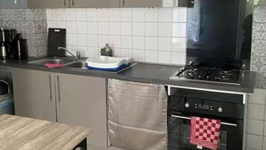 Moderni keittiö, jossa on harmaat kaapit, musta liesi ja laatoitettu välitila.