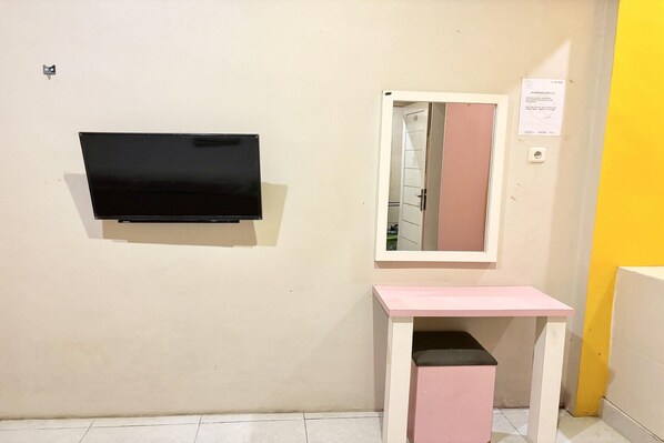 A room with a flat-screen TV mounted on the wall, a mirror with a pink frame, and a small pink table with a black top.