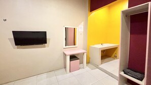 A bathroom with a flat-screen TV mounted on the wall, a mirror, a sink, and a shelf.