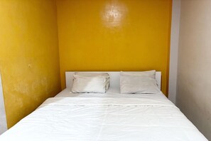 A single bed with white bedding in a room with yellow walls.