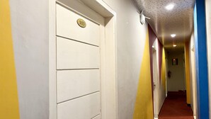Un pasillo con una puerta blanca marcada '103', una alfombra roja y paredes pintadas de amarillo y azul.