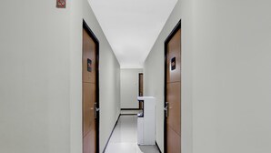 A narrow hallway with wooden doors, a white trash bin, and a sign on the wall.