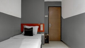 A hotel room with a bed, a wooden wardrobe, a nightstand, and a small cabinet.